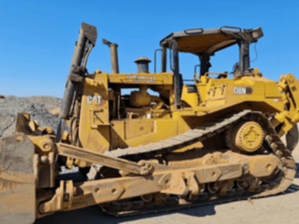 Tractor bulldozer Caterpillar modelo D8N estacionado en una obra a cielo abierto sobre terreno de grava, con cuchilla frontal y orugas cubiertas de tierra. El cielo despejado y el entorno árido indican un entorno de construcción o movimiento de tierras.