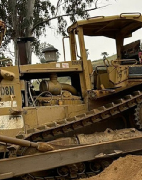 Bulldozer Caterpillar D8N trabajando en un terreno inclinado de tierra suelta, rodeado de vegetación y árboles en una zona montañosa.