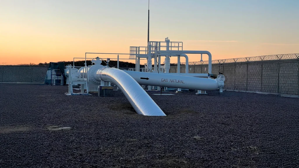 Infraestructura industrial de tubería blanca rotulada como "Gas Natural", con válvulas y componentes protegidos, al atardecer, representando los servicios de CASFAM en instalación y mantenimiento de sistemas de transporte de gas.